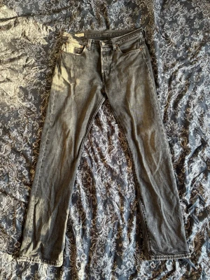 Grå Levi's 501 - Säljer ett par grå raka jeans från Levi's med klassisk femficksdesign och läderpatch bak i midjan. Jeansen har en vintage tvätt och är tillverkade i slitstark denim. Perfekta för dig som gillar en avslappnad och tidlös look.