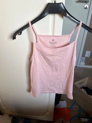 Ljusrosa ribbade linnen från H&M - Supersöta ljusrosa linnetoppar från H&M med smala axelband och ribbad struktur. Perfekt till sommaren och enkel att matcha med jeans eller kjol. Mjuka och sköna i bomullsmix, passar dig som gillar en enkel men trendig stil. Tre pack.