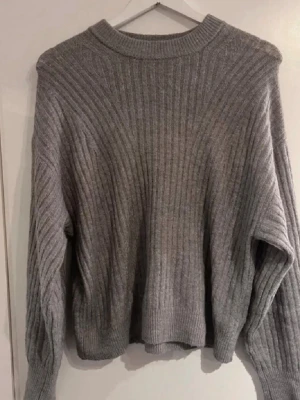 Stickad tröja - grå stickad tröja med ribbstickat mönster och rund hals. Tröjan har en avslappnad passform och långa ärmar, tröjan är stretchig