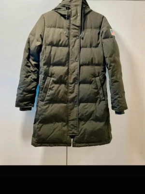 Dunjacka, som ny”, från Svea 👑  - ‼️Jackan är endast testad, och är alltså i nyskick‼️  Skön, lite längre modell i snygg khakifärg (svårt att få rätt nyans på bild), jackan är lätt figurformad vilket ger en snygg passform på 👌🏼!!  90% dun, 10% fjäder vilket gör jackan exakt lika varm som en jacka från Boomerang eller Fjällräven Expedition. Trots detta är den väldigt lätt att bära.  Passar XS-M beroende på önskad passform. Nypris 3.400:-, och jackan säljs fortfarande i butik.