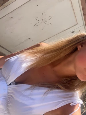 Vit topp med knytband - Säljer en vit top med djup v-ringning och knytband på axlarna.  Toppen har en luftig passform och markerad midja, perfekt för varma dagar. Tillverkad i ett lätt tyg som känns skönt mot huden.