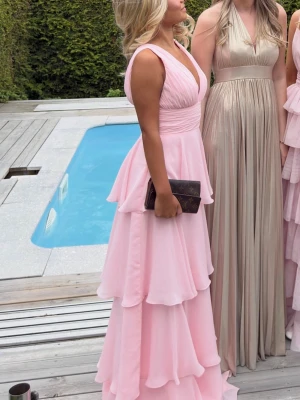 Ljusrosa balklänning med volanger - Säljer min fina balklänning, en ljusrosa långklänning med flera lager volanger och breda axelband. Klänningen har v-ringning och markerad midja som ger en snygg 