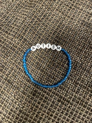 Blått pärlarmband med text - Snyggt armband med små blå pärlor och vita bokstavspärlor som stavar AUTISM. Armbandet är elastiskt och passar de flesta handleder. Perfekt accessoar för dig som vill bära ett statement och gillar färgglada detaljer.