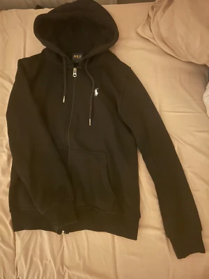 Svart hoodie från Polo Ralph Lauren - Svart hoodie från Polo Ralph Lauren med dragkedja, huva Det står att det är storlek S men den är liten och passar Xs den är också helt ny