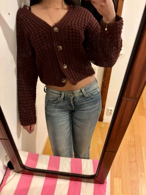 Stickad kofta med stora knappar - Säljer en grovstickad kofta med v-ringning och stora dekorativa knappar framtill. Koftan är croppad och har långa, vida ärmar. Perfekt för dig som gillar en avslappnad men trendig stil. Används fåtal gånger.