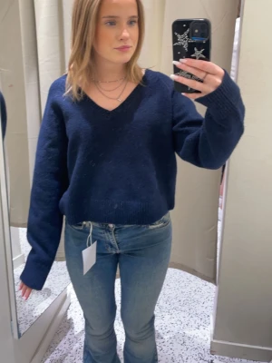 Mörkblå stickad tröja med v-ringning - En mörkblå stickad tröja från Bik Bok med v-ringad hals och långa ärmar. Tröjan har en något kortare, boxig passform och ribbstickade muddar vid ärmslut och nederkant. Perfekt för lager-på-lager och enkel att matcha.