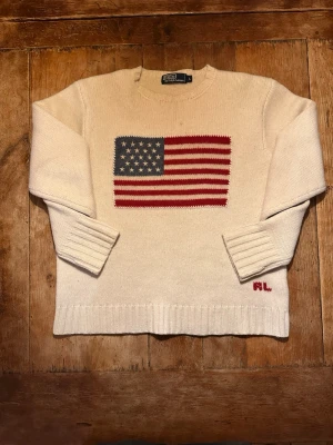 Ralph Lauren 100% Lammull I L - Ralph Lauren vit lammulströja med USA motiv. Tröjan är genuint en av de finast stickade tröjorna jag har sett, materialet är av högsta kvalitet. Tröjan är av tjock lammull. Storleken är L men i och med att det är en Unisex tröja är storleken närmare L för tjejer och M/S för killar. Hör av dig vid frågor eller prisförslag!