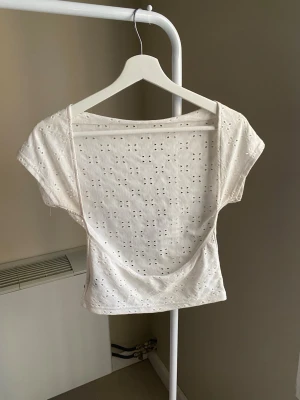 Vit broderad croppad topp - Söt vit croppad topp med broderade detaljer och öppen rygg. Toppen har korta ärmar och ett luftigt, somrigt material som känns lätt på kroppen. Perfekt för dig som gillar romantiska och feminina plagg.