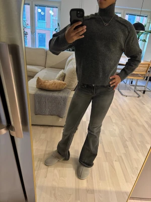 Mörkgrå polotröja i stickat - Säljer en mörkgrå stickad polotröja med hög krage och ribbade muddar. Tröjan har en avslappnad passform och är perfekt för kalla dagar. Materialet känns mjukt och värmande, och färgen är lätt att matcha med olika outfits.