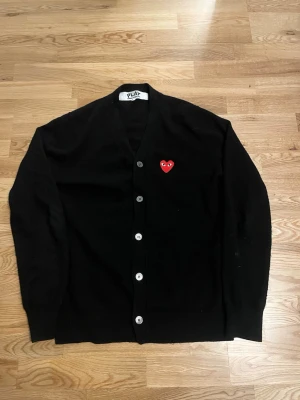 PLAY Comme des Garçons Cardigan Svart – Strl M - Säljer min PLAY Comme des Garçons cardigan i svart med röda hjärtloggan.  • Storlek: M • Färg: Svart • Skick: Väldigt bra skick • 100% ull • Köpt i Japan  Väldigt populär modell som passar till allt. Säljer pga används inte längre. Snabb affär prioriteras ⚡  Kan skickas eller mötas upp.