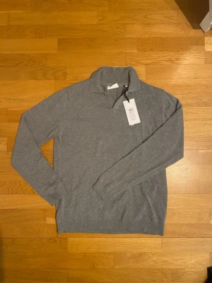 Grå stickad tröja från Lindbergh - Snygg grå långärmad pikétröja från Lindbergh. Tröjan har klassisk krage och är aldrig använd. 