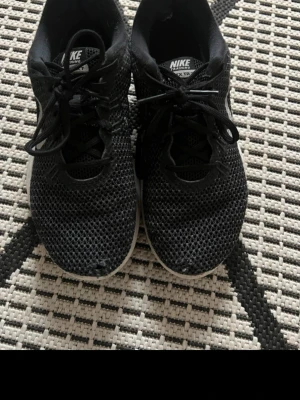 Svarta Nike sneakers mesh - Säljer ett par svarta Nike sneakers med ovandel i ventilerande mesh och vita sulor. Skorna har klassisk låg profil, snörning och diskret Nike-logga på plösen och hälen. Perfekta för en sportig och avslappnad stil.