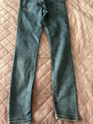 Ljusblå skinny jeans - Säljer ett par ljusblå skinny jeans med klassisk femficksdesign och normal midja. Jeansen har raka ben och är tillverkade i ett mjukt denimtyg som ger en avslappnad look. Perfekta till sneakers eller boots för en casual stil.