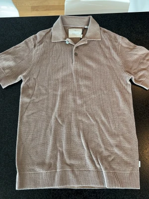 Beige kortärmad t-shirt Jack & Jones - Säljer en beige kortärmad t-shirt från Jack & Jones med diskret strukturmönster. T-shirten har klassisk krage och ribbade detaljer vid ärmslut och nederkant. Perfekt för dig som gillar stilrena plagg med lite extra känsla.