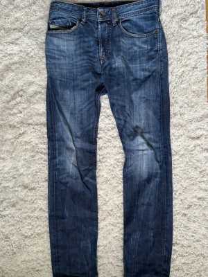 Diesel Industry jeans - Säljer ett par blå slim fit jeans med snygga slitningar på bakfickorna och tvättade detaljer. Klassisk femficksmodell med knappgylf och kontrastsömmar. Jeansen har en modern passform och är perfekta för en avslappnad stil. Materialet är denim i bomull. Uppskattad storlek