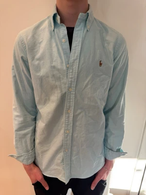 Ljusblå Ralph Lauren Skjorta - Säljer en för fet ljusblå Polo Ralph Lauren skjorta i storlek S. Modellen är 181 cm och väger 66kg