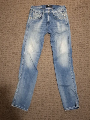 Ljusblå slim fit jeans Replay - Säljer ett par ljusblå Replay jeans. Jeansen har fem fickor, passform slim fit, storlek 27W 32L. Materialet är mjukt denim med stretch för extra komfort. Perfekta för en avslappnad och trendig look. Är köpta från Åhlens för 1500 kr.