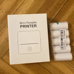 Mini bärbar skrivare med papper - Säljer en vit mini bärbar skrivare i plast med USB-kabel och flera rullar termopapper. Perfekt för att snabbt skriva ut små lappar, etiketter eller anteckningar direkt från mobilen. Enkel och smidig design, lätt att ta med sig överallt.