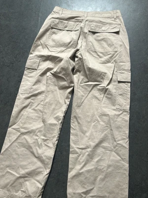 Beige cargobyxor med stora fickor - Säljer ett par beige cargobyxor med bred passform och flera stora fickor på sidorna och baktill. Byxorna har en avslappnad look och är tillverkade i ett mjukt bomullstyg. Perfekta för dig som gillar streetwear och praktiska detaljer.