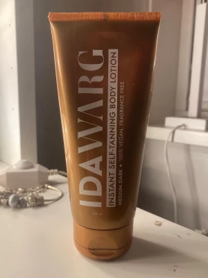 IDA WARG brun utan sol lotion - Instant self-tanning body lotion från IDA WARG i färgen medium dark. Tuben är kopparfärgad med vit text och innehåller 200 ml. Produkten är 100% vegansk och doftfri, perfekt för dig som vill ha en naturlig solkysst look utan sol.