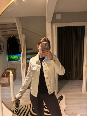 Vit jeansjacka med klassisk passform - Snygg vit jeansjacka med klassisk krage, knäppning framtill och två bröstfickor med lock. Jackan har en rak och något kortare passform som ger en trendig look. Perfekt att slänga över en hoodie eller t-shirt för en cool vardagsstil.