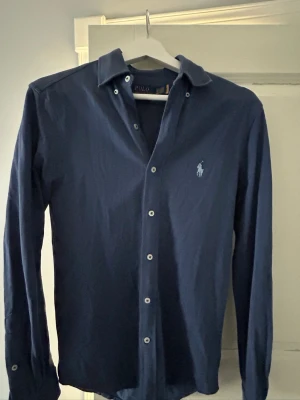 Marinblå skjorta från Polo Ralph Lauren - En marinblå skjorta från Polo Ralph Lauren! Använd bara ett fåtal gånger. Storleken är XS, passar S också. Köpt i en Ralph Lauren butik i Mallorca. Nypris ligger runt 1699kr. Mitt pris 649kr! Priset är ej hugget i sten. Hör av er vid funderingar!