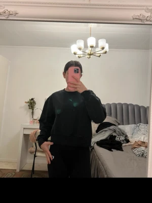 Svart oversized hoodie - En svart oversized hoodie med klassisk rund halsringning och ribbade muddar vid ärmslut och nederkant. Hoodien är enkel och stilren utan synliga loggor eller tryck, perfekt för en chill och avslappnad look. Materialet ser ut att vara mjukt och bekvämt, troligen bomull eller bomullsblandning.