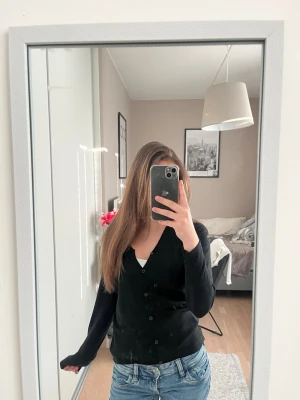 Svart basic kofta med knappar - Enkel svart kofta med långa ärmar och knäppning framtill. Snygg och stilren modell som passar till det mesta. Perfekt att slänga över ett linne eller t-shirt för en avslappnad look.