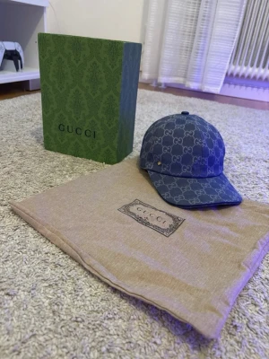 Blå keps - Säljer en blå keps har böjd skärm och en liten guldfärgad detalj på sidan. Perfekt för dig som vill ha en exklusiv och trendig accessoar.