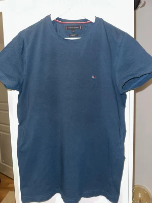 Marinblå t-shirt från Tommy Hilfiger - Snygg marinblå t-shirt från Tommy Hilfiger i ekologisk bomull. Slim fit-modell med korta ärmar och rund hals. Liten klassisk Hilfiger-logga broderad på bröstet. Perfekt basplagg för en clean och stilren look.