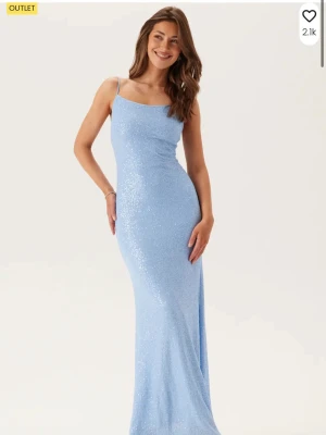 Ljusblå glittrig balklänning  - Elegant ljusblå långklänning med smala axelband och öppen rygg med knyt. Klänningen har en glittrig yta som fångar ljuset och en figurnära passform som framhäver siluetten. Perfekt för speciella tillfällen där du vill sticka ut.