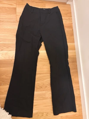 Svarta kostymbyxor från BikBok - Snygga svarta kostymbyxor från BikBok med klassisk rak passform och hällor för skärp. Byxorna har dragkedja och knappstängning framtill. Perfekta för en clean och stilren look.
