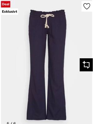 Marinblå Roxy linnebyxor - Snygga marinblå linnebyxor från Roxy med raka ben och avslappnad passform. Byxorna har ett vitt dragsnöre i midjan, resår och bakfickor. Tillverkade i ett luftigt linnematerial som passar perfekt till sommaren.