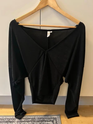 Svart v-ringad topp från NELLY - Trendig svart topp från NELLY med djup v-ringning och lång ärm. Toppen har en loose passform och är tillverkad i mjukt, stretchigt material som ger en snygg siluett. Perfekt att styla med både jeans och kjol.