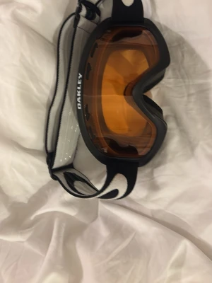 Oakley skidglasögon svart/orange - Säljer ett par Oakley skidglasögon med svart ram och orange tonade linser. Bredt elastiskt band med vit och svart Oakley-logga. Perfekta för skidåkning eller snowboard och ger bra skydd mot vind och snö.