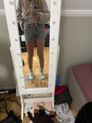 Gråa högmidjade jeansshorts - Säljer ett par gråa högmidjade jeansshorts med broderade detaljer på baksidan. Shortsen har en klassisk femficksdesign och råa kanter vid bensluten. Perfekta för sommaren och ger en cool vintagekänsla.