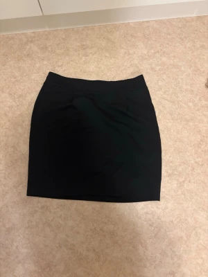 Svart kortkjol i stretchigt tyg - Enkel och stilren svart kortkjol i stretchigt material. Kjolen har en rak passform och resår i midjan för extra komfort. Perfekt att matcha med en crop top eller oversized tröja för en trendig look.