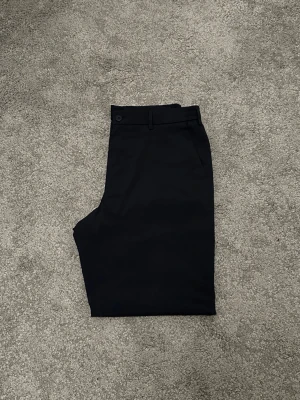 Mörkblå chinos med rak passform - Snygga mörkblå chinos med rak passform och klassisk design. Byxorna har bälteshällor, knappstängning och sidofickor. Perfekta för en clean och stilren look. Materialet känns lättsamt, mjukt och följsamt.