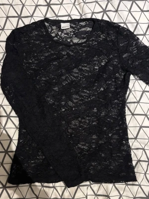 Svart spetsblus från Gina Tricot - Säljer en svart långärmad spetsblus från Gina Tricot. Toppen är helt i genombruten spets med blommigt mönster och har en tight passform. 