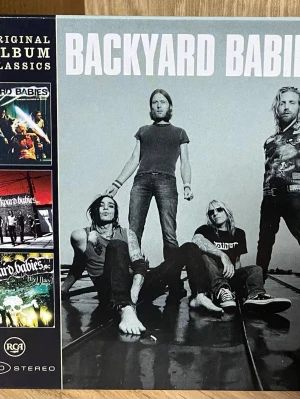 Backyard Babies Original Album Classics - Samling med tre album av Backyard Babies i box: Making Enemies Is Good, Stockholm Syndrome och Live Live In Paris. Omslaget har svartvita och färgade bilder på bandet och albumens låtlistor syns på baksidan. Perfekt för dig som gillar rock och samlar på CD-boxar.