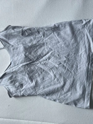 Ljusgrå linnetopp med smala axelband - Säljer 3 linnetoppar, 2 svarta 1 vit, med smala axelband och v-ringad hals. Toppen har en rak passform och är tillverkad i mjukt bomullsmaterial. Perfekt att matcha med jeans eller kjol för en clean look. Spännerna är sönder men det går att spänna ändå bara att de kan åka ner