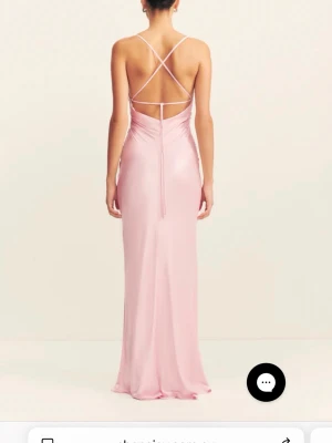 Ljusrosa långklänning med öppen rygg - Elegant ljusrosa långklänning i satinliknande material med smala axelband och snygg öppen rygg med korsade band. Klänningen har figurnära passform och lätt rynkade detaljer framtill. Perfekt för dig som vill sticka ut på bal eller fest. Den är i amerikansk storlek 2 men den passar mig som har storlek S och är 173 cm lång!🩷
