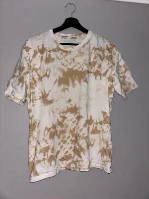 Beige tie-dye t-shirt Tiger of Sweden - Säljer en beige och vit tie-dye t-shirt från Tiger of Sweden. T-shirten har korta ärmar, rund halsringning och är tillverkad i mjuk bomull. Diskret logga på bröstet. Perfekt för en avslappnad och trendig look.