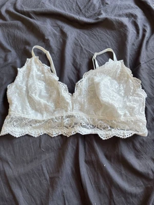 Vit spetsbralette med smala band - Säljer en vit bralette i spets med tunna axelband och dekorativ kant nertill. Bh:n har triangelformade kupor och är helt i spets med mjuk insida. Perfekt för dig som gillar en feminin och bekväm stil.