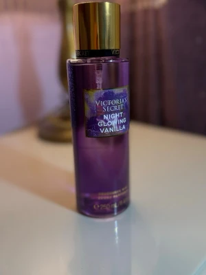 Victoria's Secret Night Glowing Vanilla - En snygg parfymflaska från Victoria's Secret i lila plast med guldig kork. Doften heter Night Glowing Vanilla och flaskan rymmer 250 ml. Perfekt för dig som gillar söta och varma vaniljtoner.