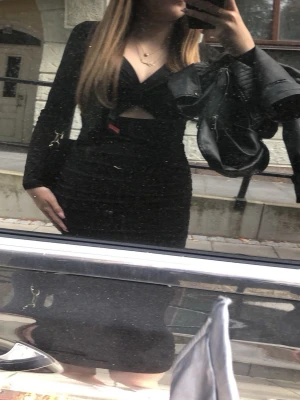 Svart kort klänning med cut-out - Säljer en svart, tight klänning med lång ärm och v-ringad hals. Klänningen har en snygg cut-out detalj framtill som ger en cool look. 