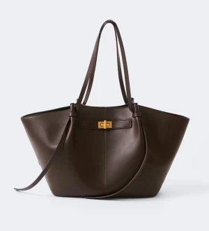 Brun shoppingväska i läderlook - Stilren brun shoppingväska med rymlig design och dubbla axelband. Väskan har en elegant guldfärgad vridknäppning framtill och är tillverkad i ett slätt material som liknar läder. Perfekt för dig som vill ha plats med allt du behöver under dagen.