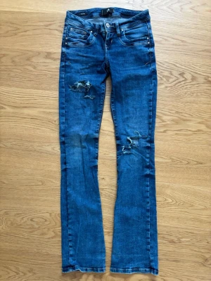 Blå slitna jeans från LTB valerie  - Säljer ett par blå jeans från LTB, modell Valerie. Jeansen har slitningar och hål på låret och knät. Klassisk femficksmodell med knappgylf och raka ben. Storlek 25/34. 
