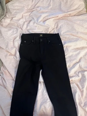 Svarta jeans från Lee - Snygga svarta jeans från Lee med klassisk femficksdesign och raka ben. Jeansen har bälteshällor och Lee-logga på bakfickan. Perfekta till många olika outfits och enkla att matcha. Passar en med storlek xs/ s