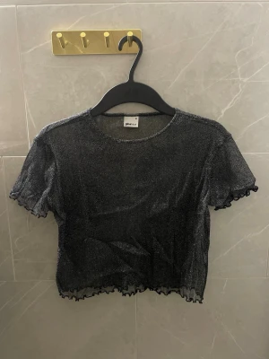 Glittrig croppad mesh topp  Gina -  Toppen har korta ärmar och vågig kant vid ärmslut och nederkant.